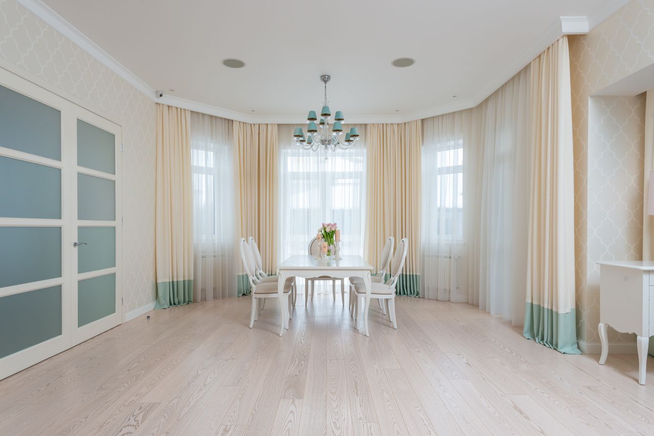 our-services-01 Interior of light apartment room with white wooden table near chairs next to windows with curtains in daylight