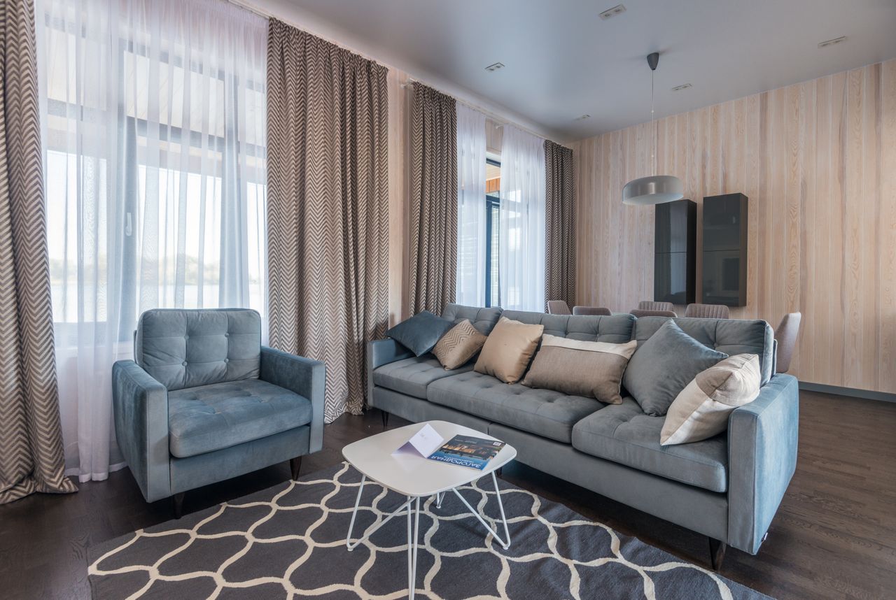 Elegant living room with blue sofa, armchair, and patterned curtains creating a cozy atmosphere.
