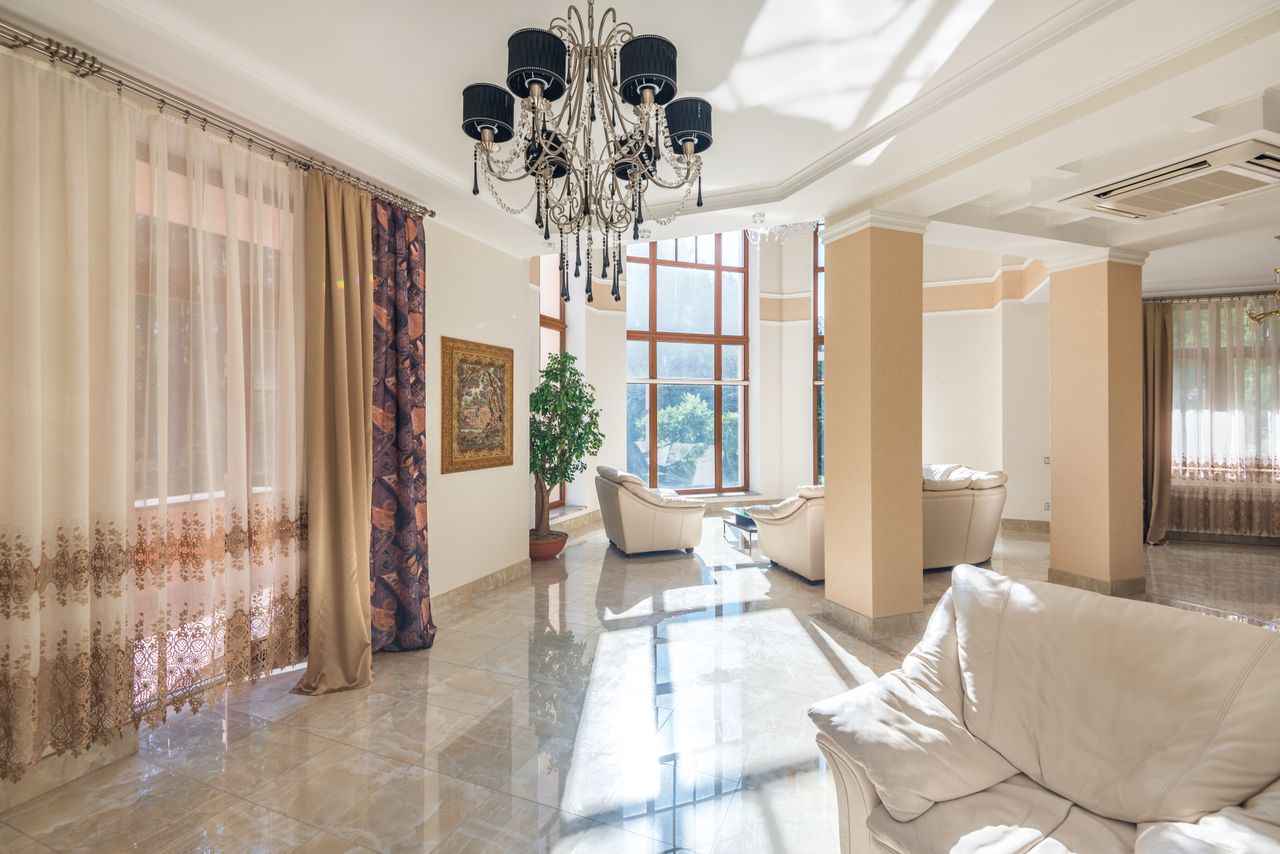 our-services-01 Spacious living room featuring elegant chandelier, large windows, and plush seating.